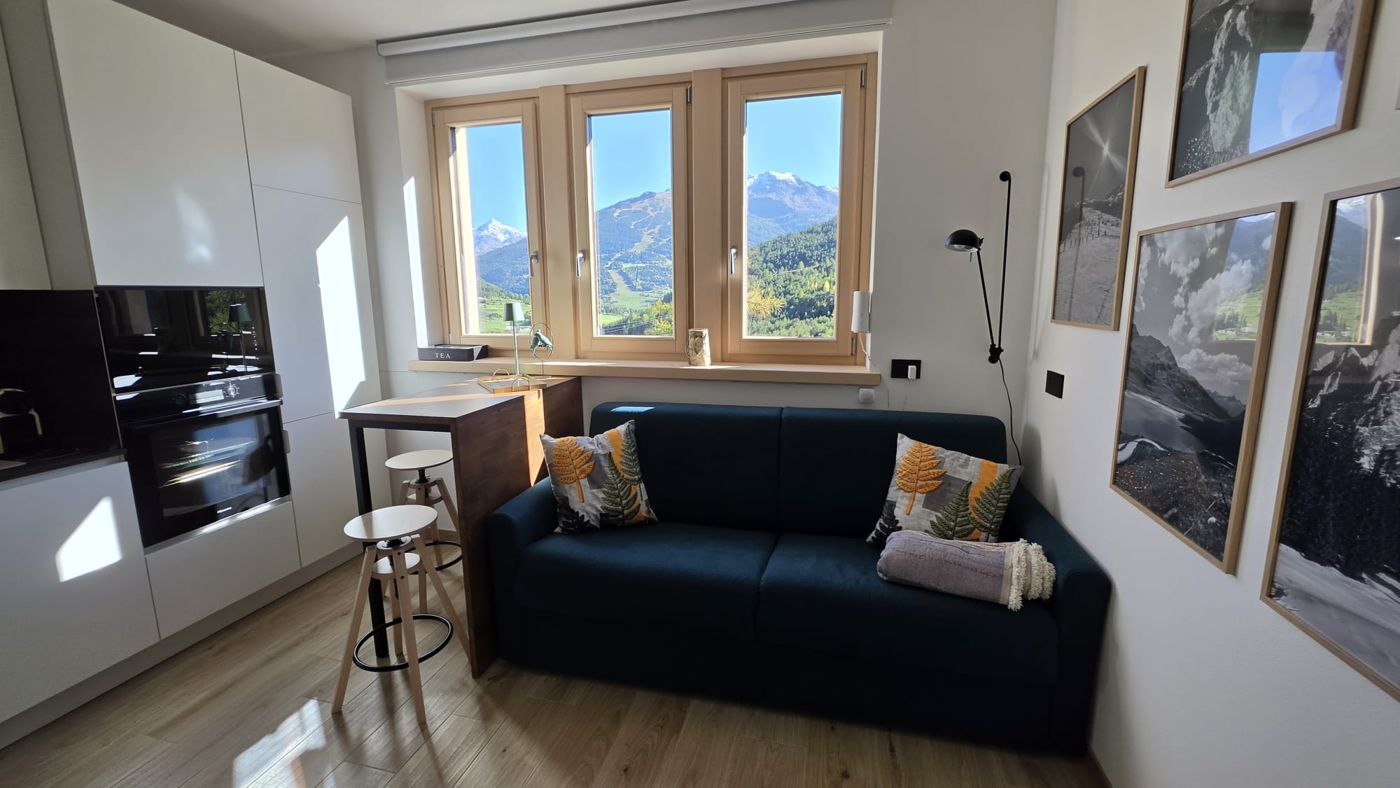 The living room with sofa bed, kitchenette and three windows facing the mountains